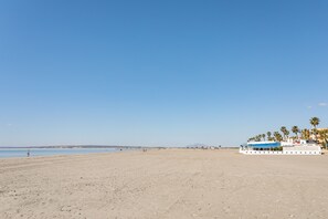 Una playa con un barco grande, palmeras y cielo despejado.