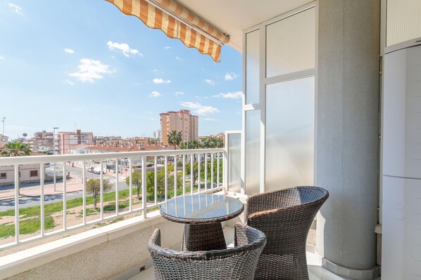 Un balcón con mobiliario de mimbre, vista panorámica de la ciudad y un edificio al fondo.