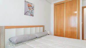 Un lit bien fait, avec une tête de lit, un tableau accroché au mur et une armoire en bois.