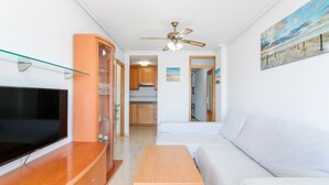 Un salon moderne doté d’un téléviseur à écran plat, de meubles en bois, d’un ventilateur de plafond et d’un tableau représentant une scène de plage.