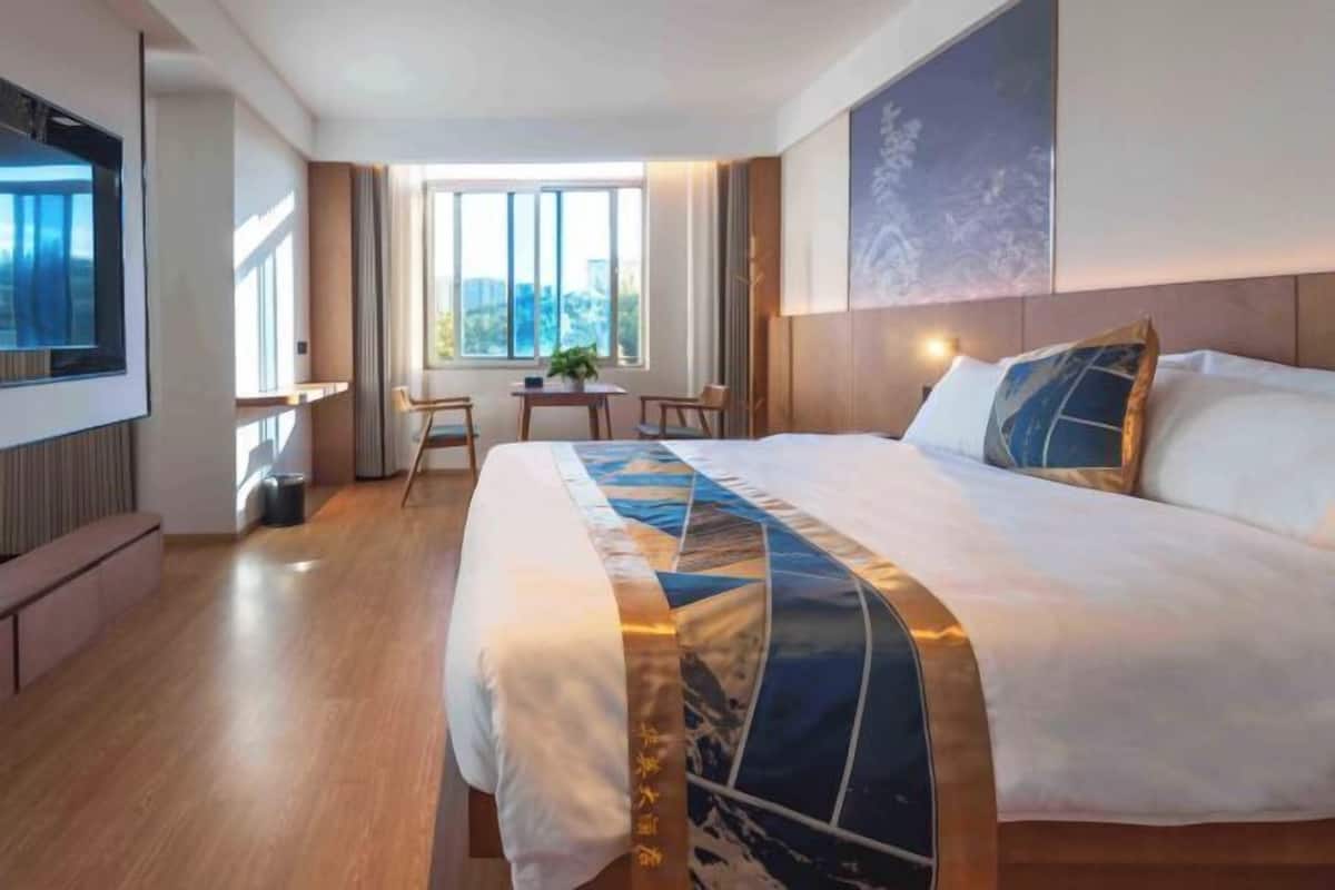 Une chambre d’hôtel avec un grand lit, un bureau, une chaise et une fenêtre donnant sur un beau paysage.