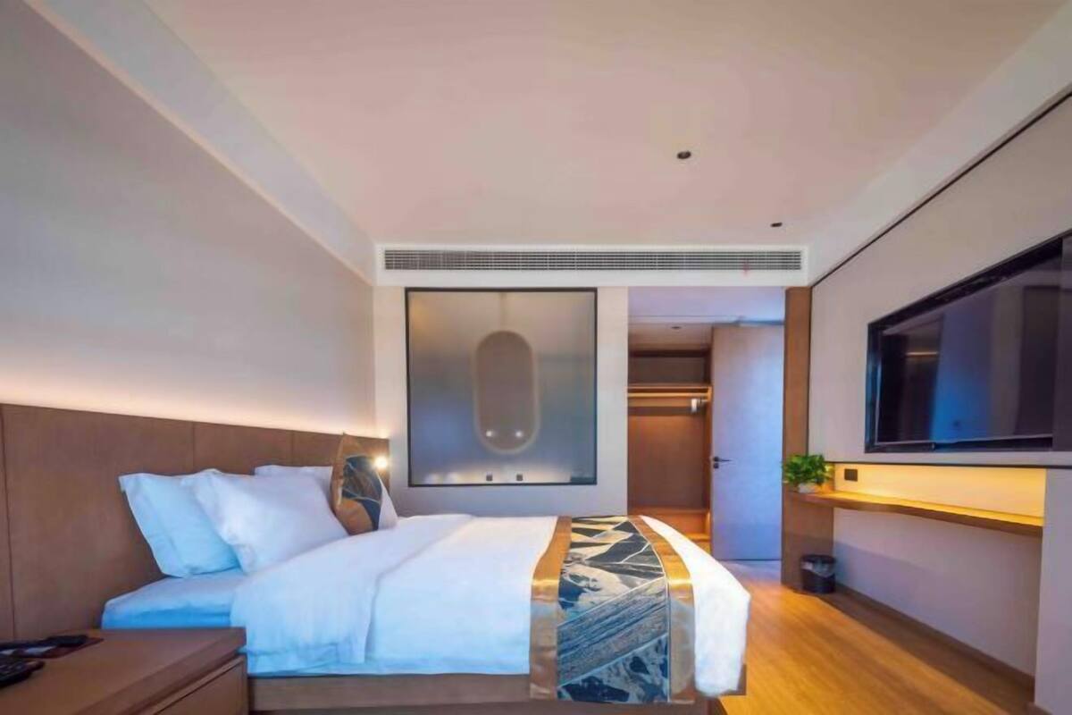 Une chambre d’hôtel moderne dotée d’un grand lit, d’une télévision et d’une porte coulissante donnant accès à la salle de bain.