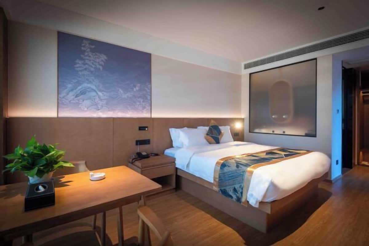 Une chambre d’hôtel moderne, équipée d’un lit, d’une table de chevet, d’une lampe et d’une grande œuvre d’art accrochée au mur.