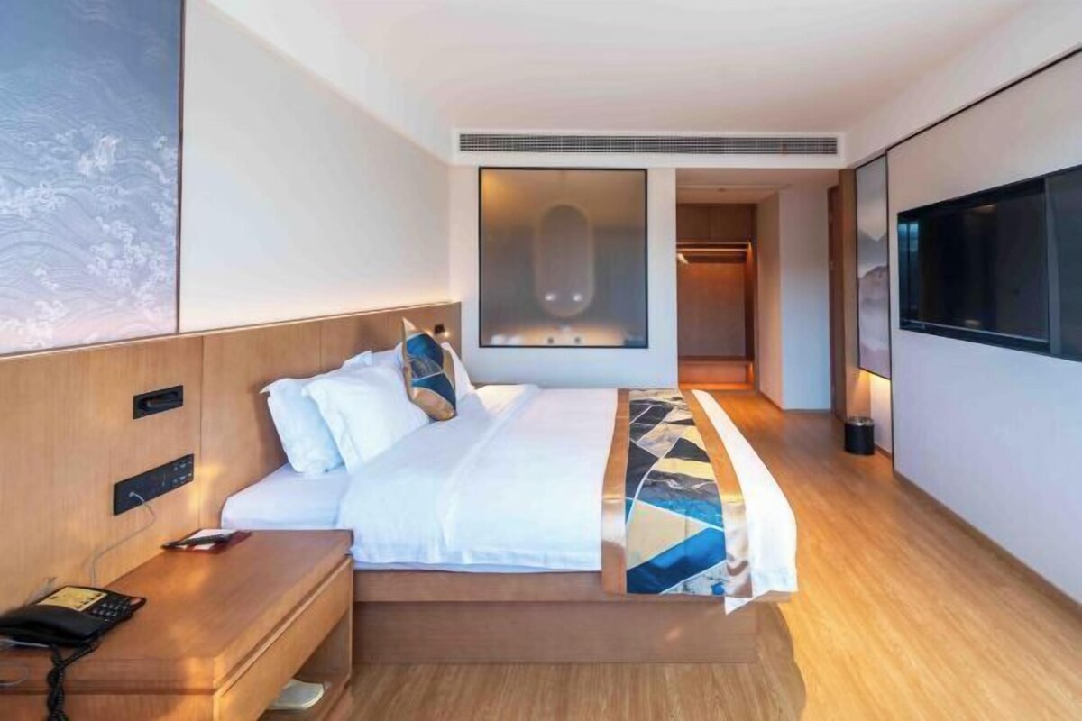 A hotel room with a bed, bedside table, and a TV mounted on the wall.