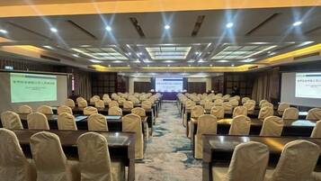 A conference room with rows of tables and chairs, a carpeted floor, and a presentation screen at the front.