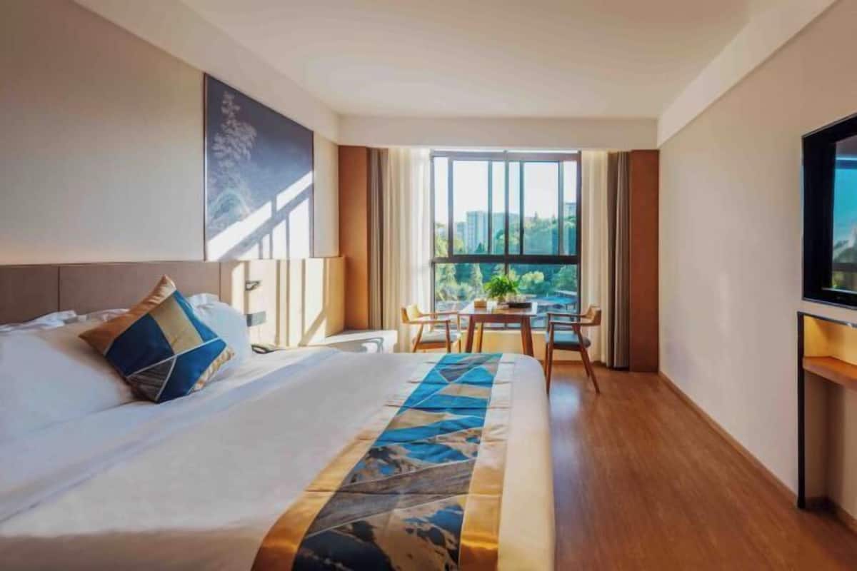 Une chambre d’hôtel avec un grand lit, un coin repas avec une table et des chaises, et une fenêtre donnant sur des immeubles.