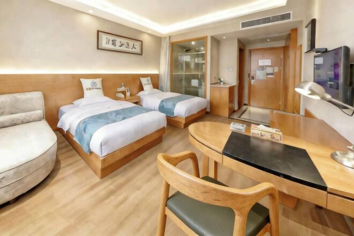 Habitación de hotel con dos camas, un escritorio, una silla, un televisor y un cuadro en la pared.