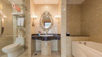 Un baño con pared de mármol, inodoro blanco, lavamanos con espejo y bañera.