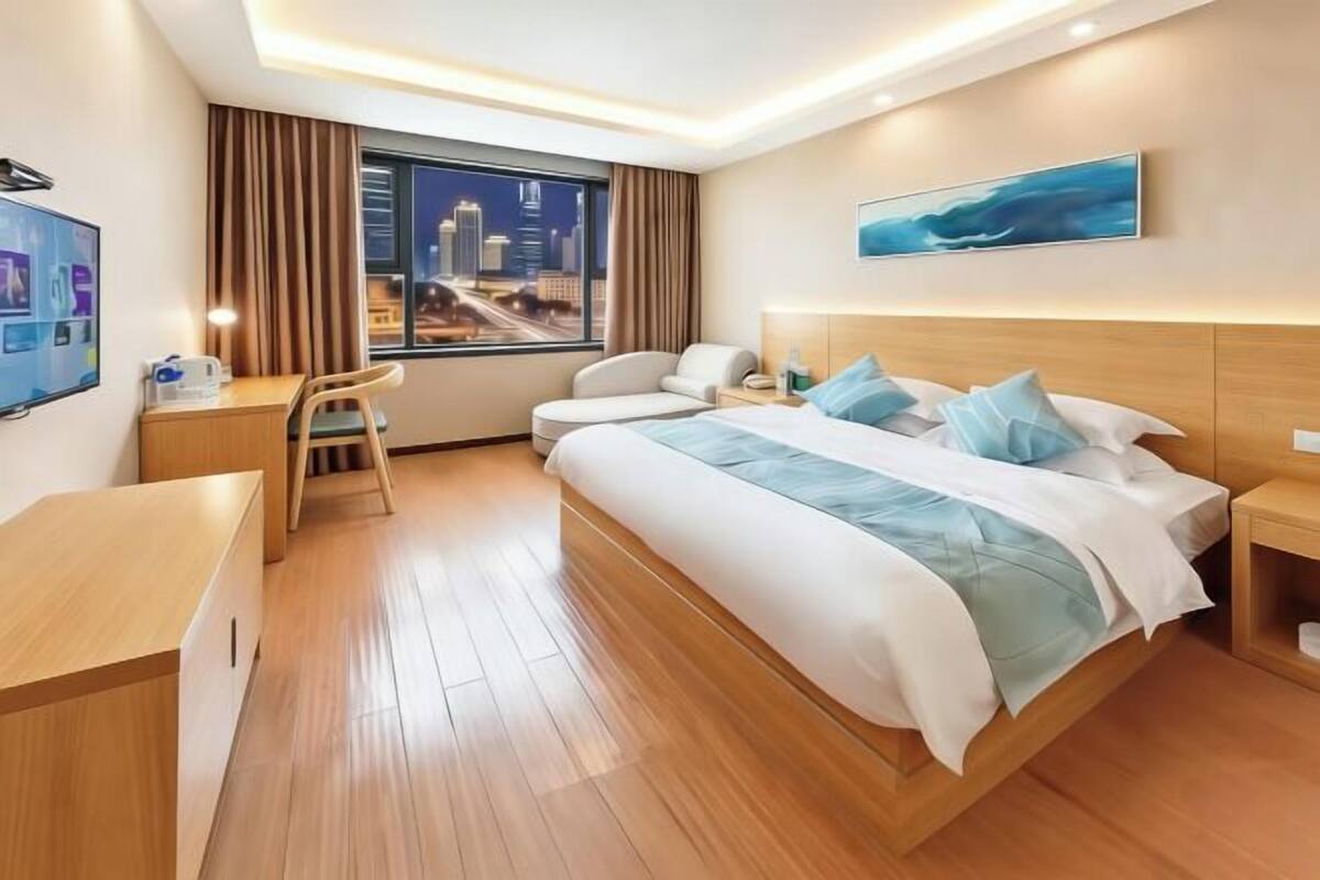 Una habitación de hotel moderna con una cama grande, un escritorio, una silla y vistas a la ciudad de noche.