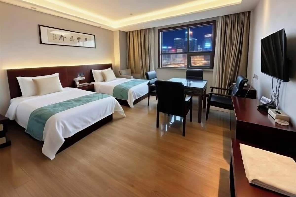 Habitación de hotel con dos camas, un escritorio, una silla, un televisor y una ventana con vistas a la ciudad.