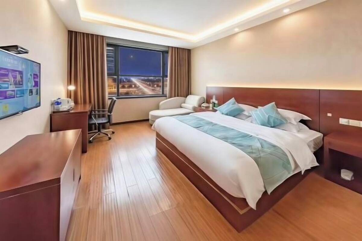 Habitación de hotel con una cama grande, un escritorio, una silla, un televisor y una ventana con vistas a la ciudad.