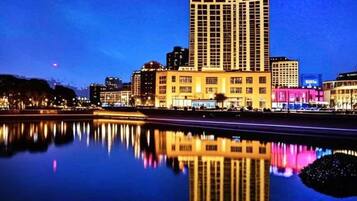 Un edificio alto con su reflejo en aguas tranquilas, rodeado de otros edificios.