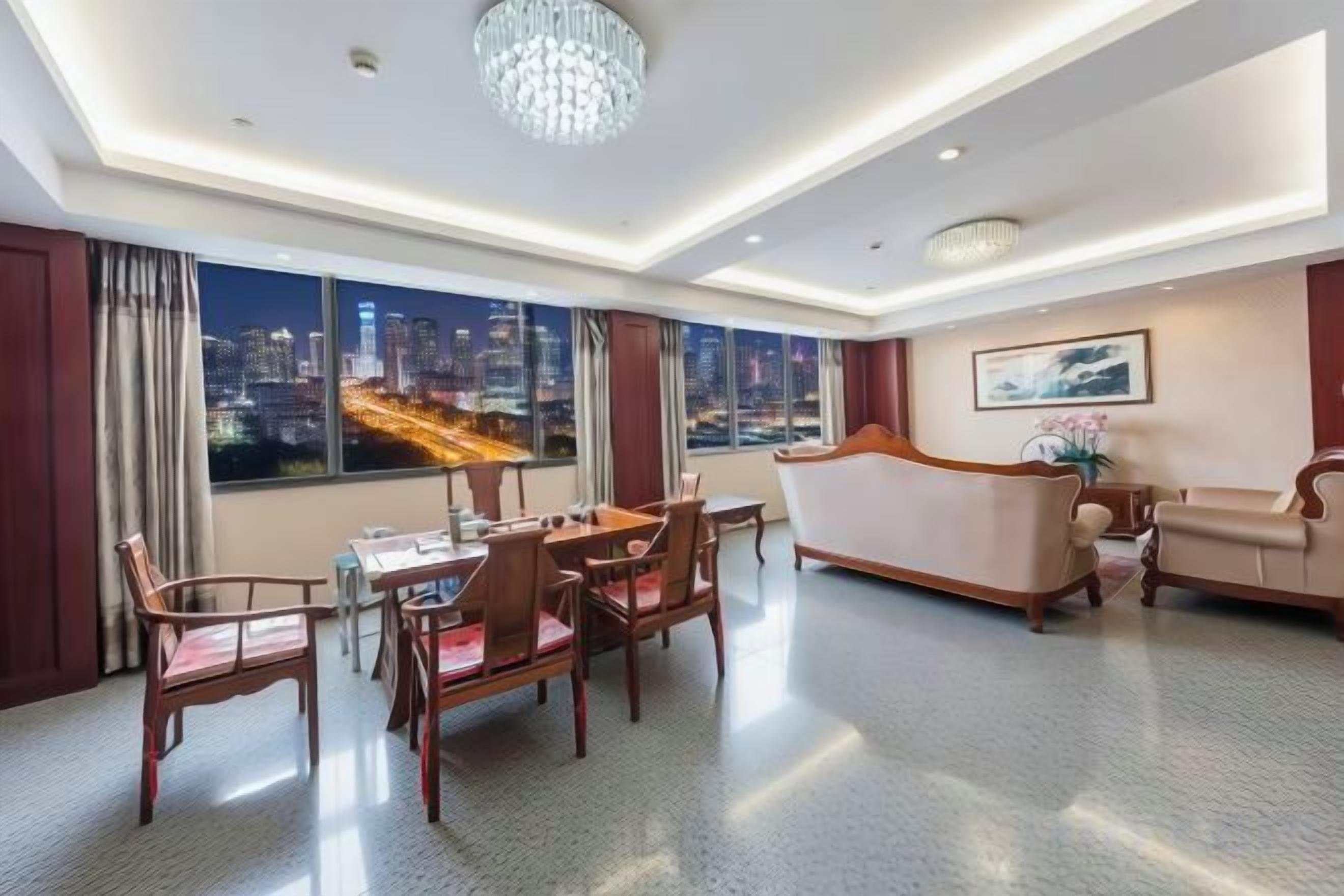 A hotel room with a dining area, a sofa, and a large window with a city view.