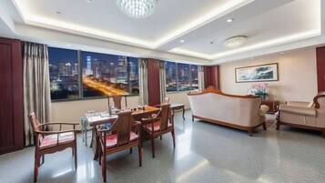 A hotel room with a dining area, a sofa, and a large window with a city view.
