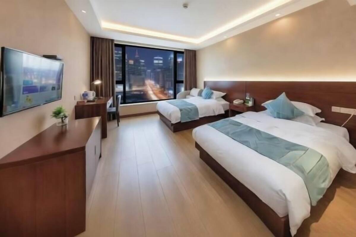Una habitación de hotel con dos camas, televisor, escritorio y un ventanal con vista a la ciudad.
