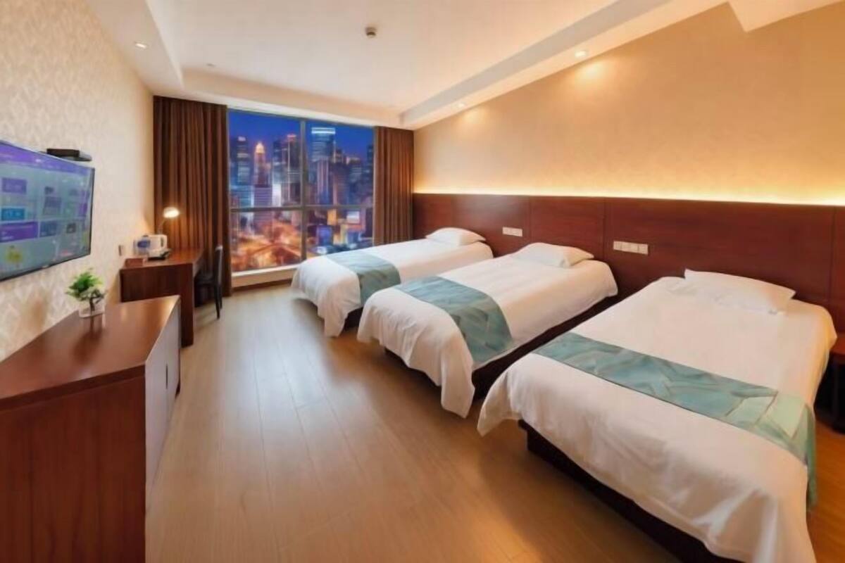 Habitación de hotel con dos camas, un escritorio, un televisor y una ventana con vista a la ciudad.