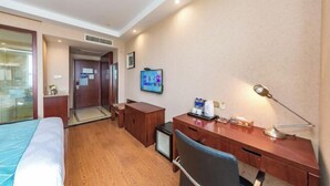 Habitación de hotel con cama, escritorio, silla, televisor y una mesita de noche con lámpara.