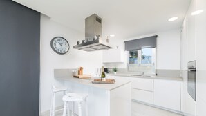 Une cuisine moderne dotée d’un îlot central, de meubles blancs, d’un four encastré et d’une grande fenêtre.