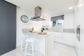 Una cocina moderna con una isla central, armarios blancos, horno integrado y un ventanal grande.