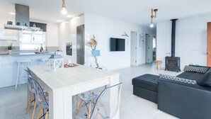 Une cuisine moderne avec un îlot central, un coin repas avec des chaises, un canapé noir et une petite table en bois avec un téléviseur.