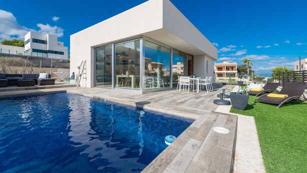 Une maison moderne dotée d’une piscine, d’un espace salon extérieur et surplombant un ciel d’un bleu éclatant.