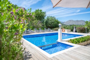 Une piscine entourée de chaises longues, avec une végétation luxuriante et des montagnes en toile de fond.