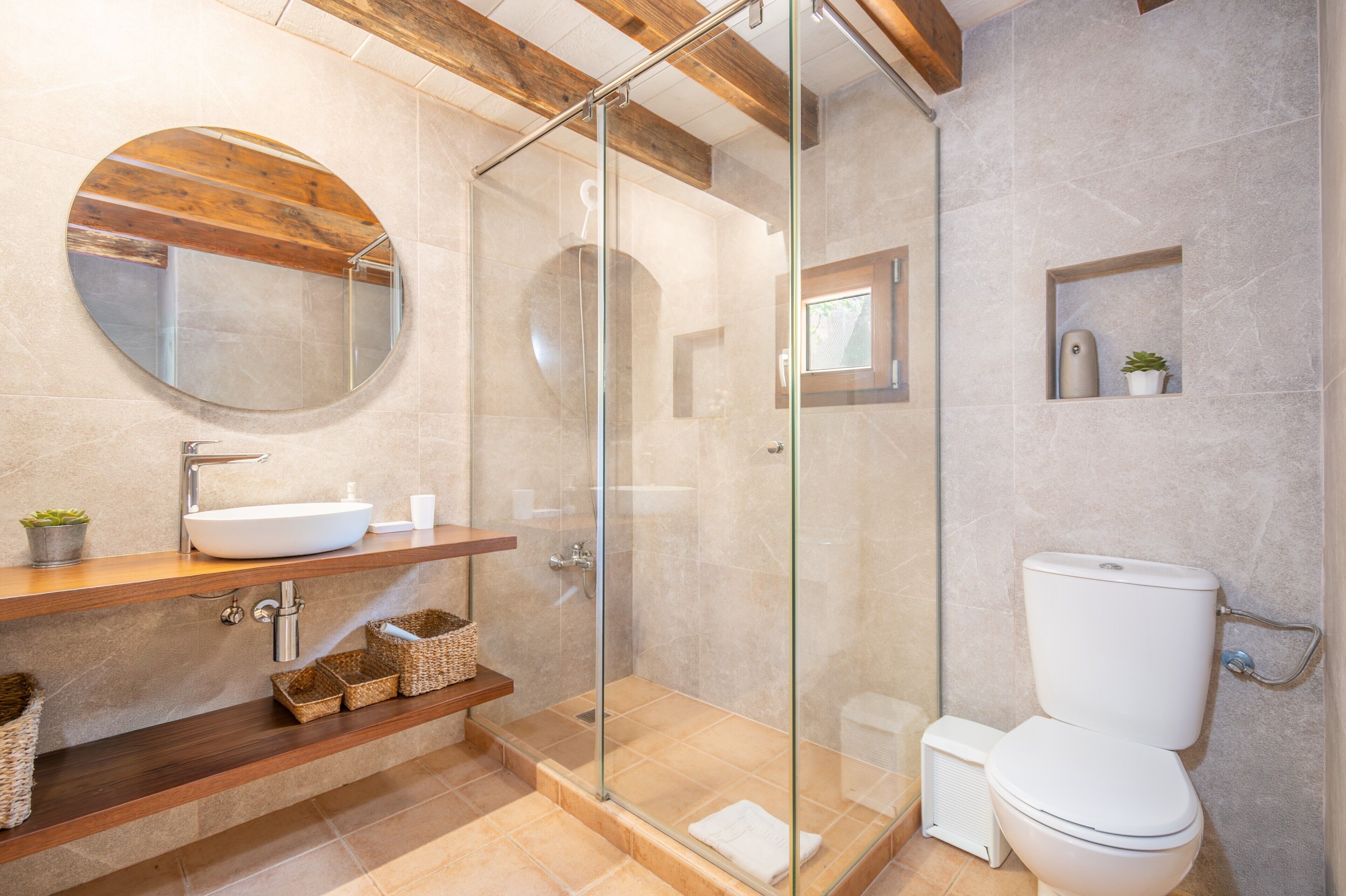 Une salle de bain avec une douche à parois de verre, un miroir rond, un lavabo blanc et des toilettes.