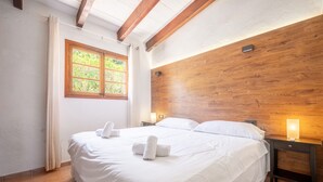 Ein Schlafzimmer mit einem hölzernen Kopfteil, einem großen Bett mit weißer Bettwäsche, zwei Nachttischlampen und einem Fenster mit Vorhängen.