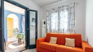 Een interieur met een bank, een deur naar een buitenruimte en een raam met gordijn.