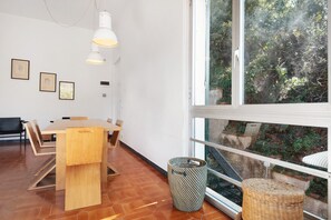 Un intérieur moderne avec une table à manger en bois, des chaises, un luminaire suspendu et une grande fenêtre donnant sur un paysage verdoyant.