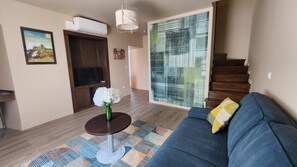 A living room with a sofa, a small round table with a vase, a television, and a staircase.