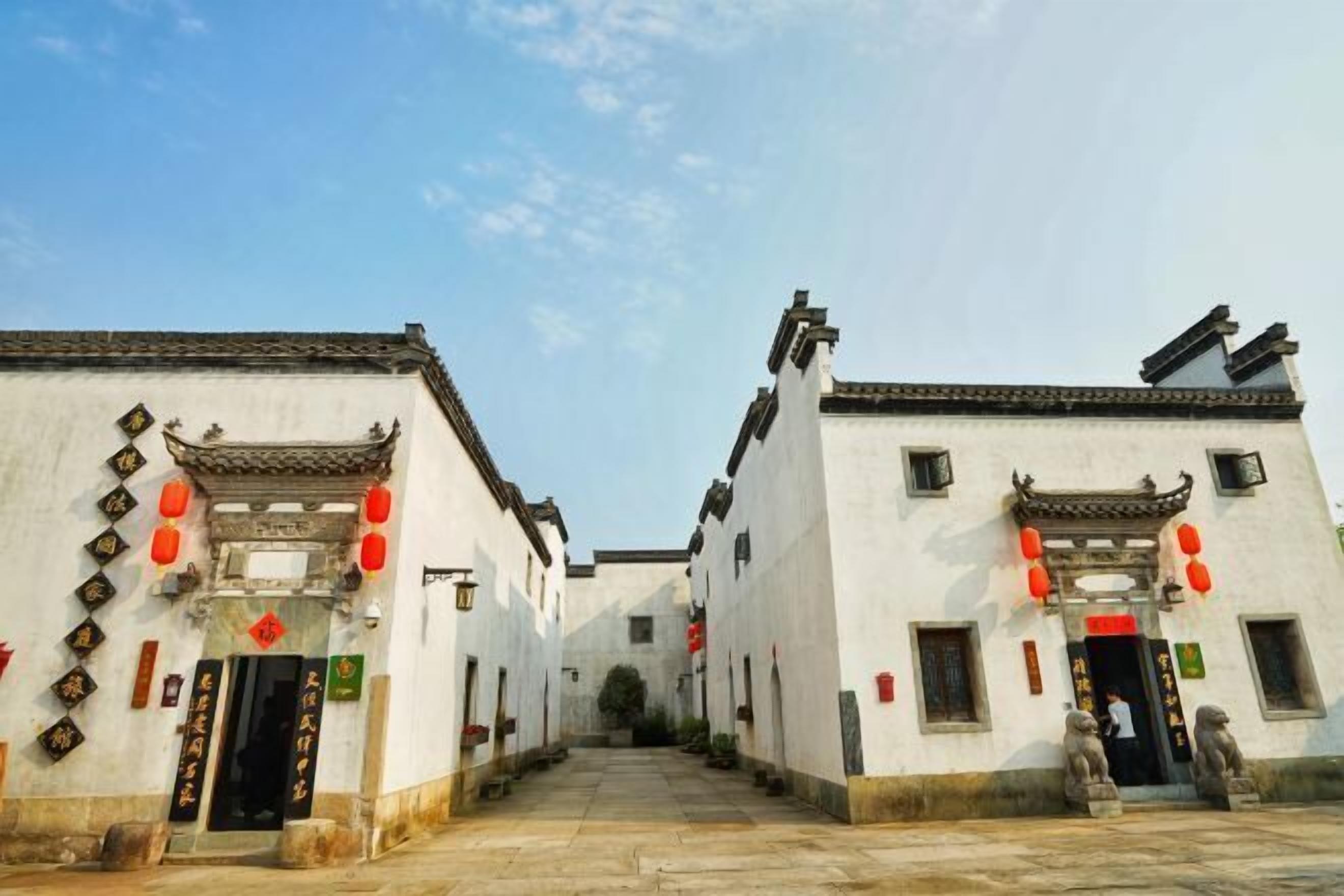 A traditional courtyard with white buildings, red lanterns, and stone lion statues.