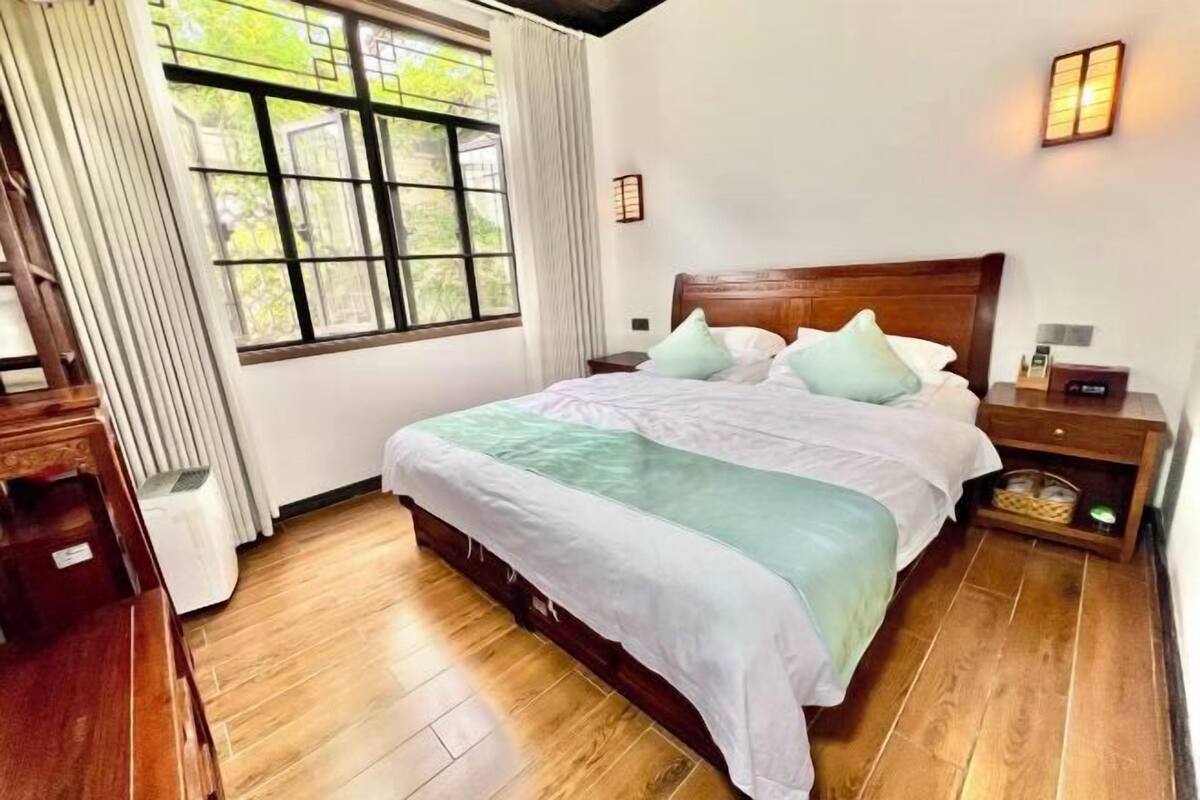 Quarto com cama de madeira, mesa de cabeceira, luminária e janela com cortinas.