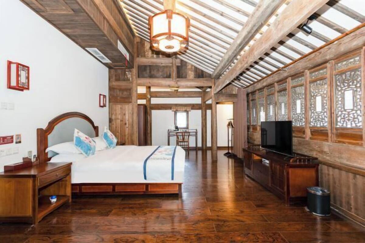 Quarto espaçoso com uma cama grande, vigas de madeira, televisão e um tradicional ecrã chinês na parede.