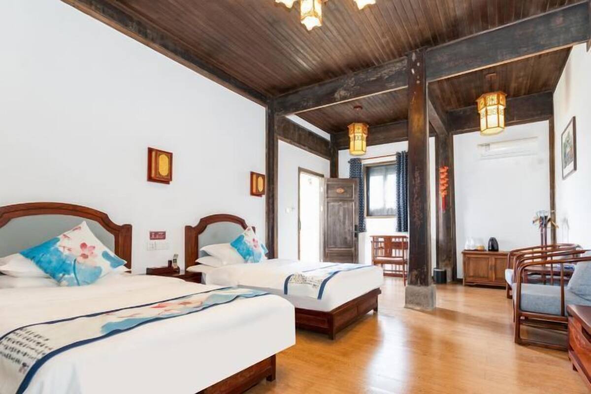 Quarto de hotel com duas camas, vigas de madeira e um espaço de estar com cadeiras.