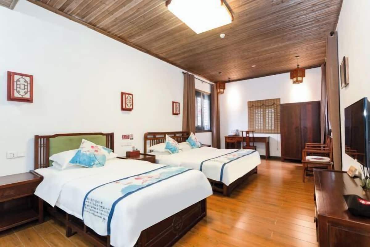 Quarto de hotel com duas camas, piso de madeira, escrivaninha e televisão.