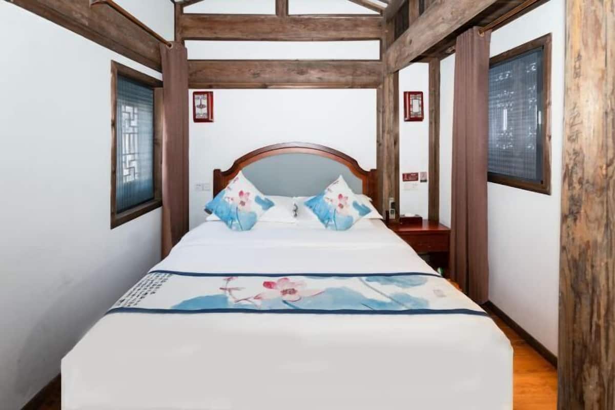 Uma cama com colcha floral, vigas de madeira e janela com persianas.