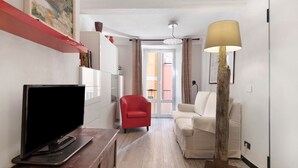 Un saló amb una televisió de pantalla plana, una cadira vermella, un sofà blanc, una làmpada i un quadre a la paret.