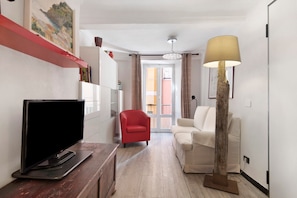 Un salon avec un téléviseur à écran plat, un fauteuil rouge, un canapé blanc, une lampe et un tableau accroché au mur.