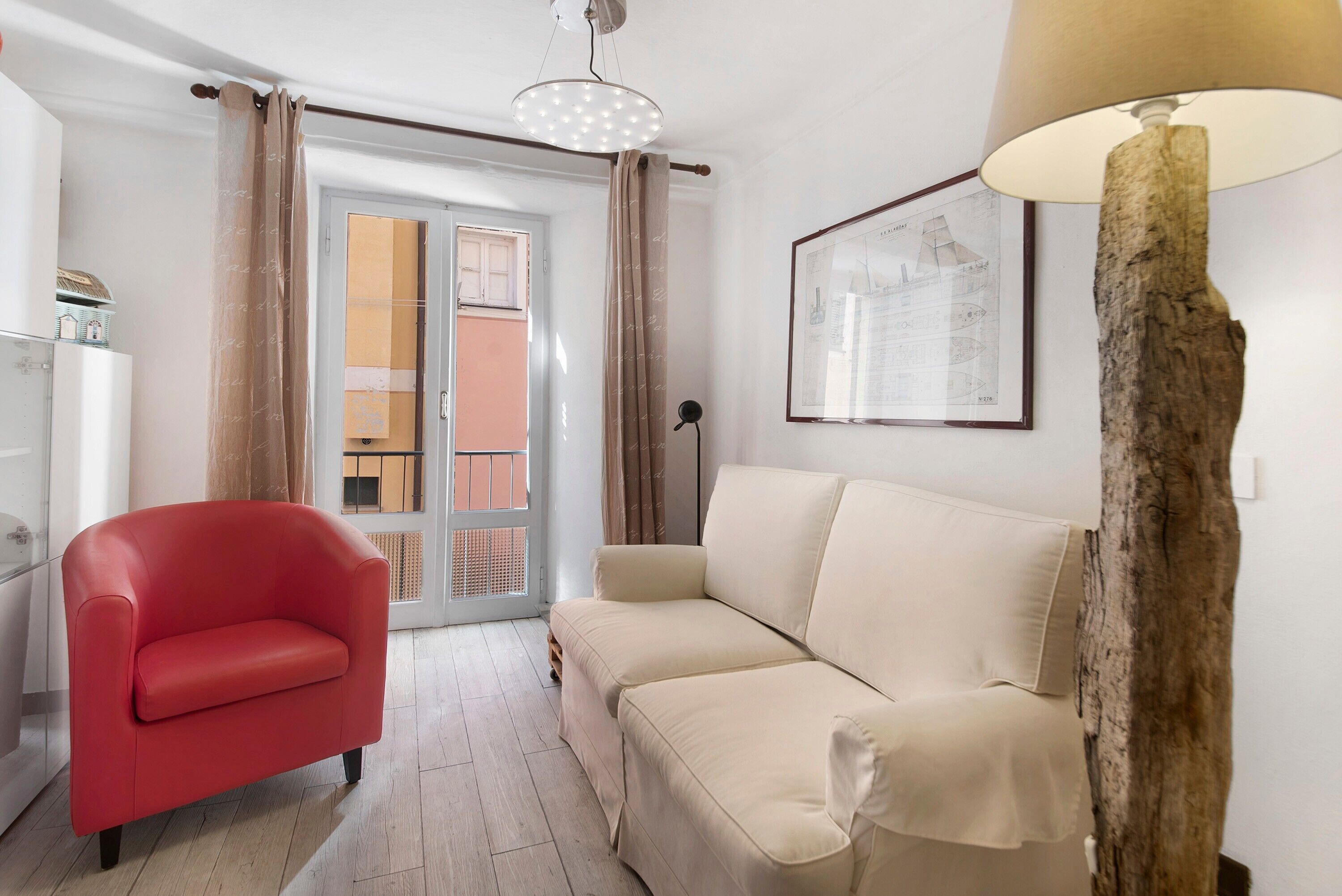 Ein Wohnzimmer mit einem roten Sessel, einem beigen Sofa, einer Holzlampe und einer gerahmten architektonischen Zeichnung an der Wand.
