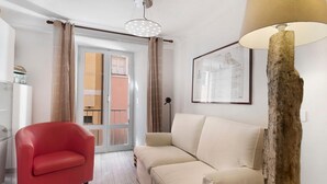 Un saló amb una poltrona vermella, un sofà beix, una làmpada de fusta i un dibuix arquitectònic emmarcat a la paret.