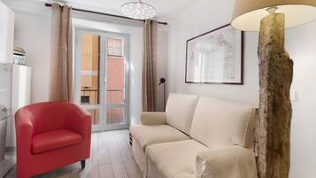 Ein Wohnzimmer mit einem roten Sessel, einem beigen Sofa, einer Holzlampe und einer gerahmten architektonischen Zeichnung an der Wand.