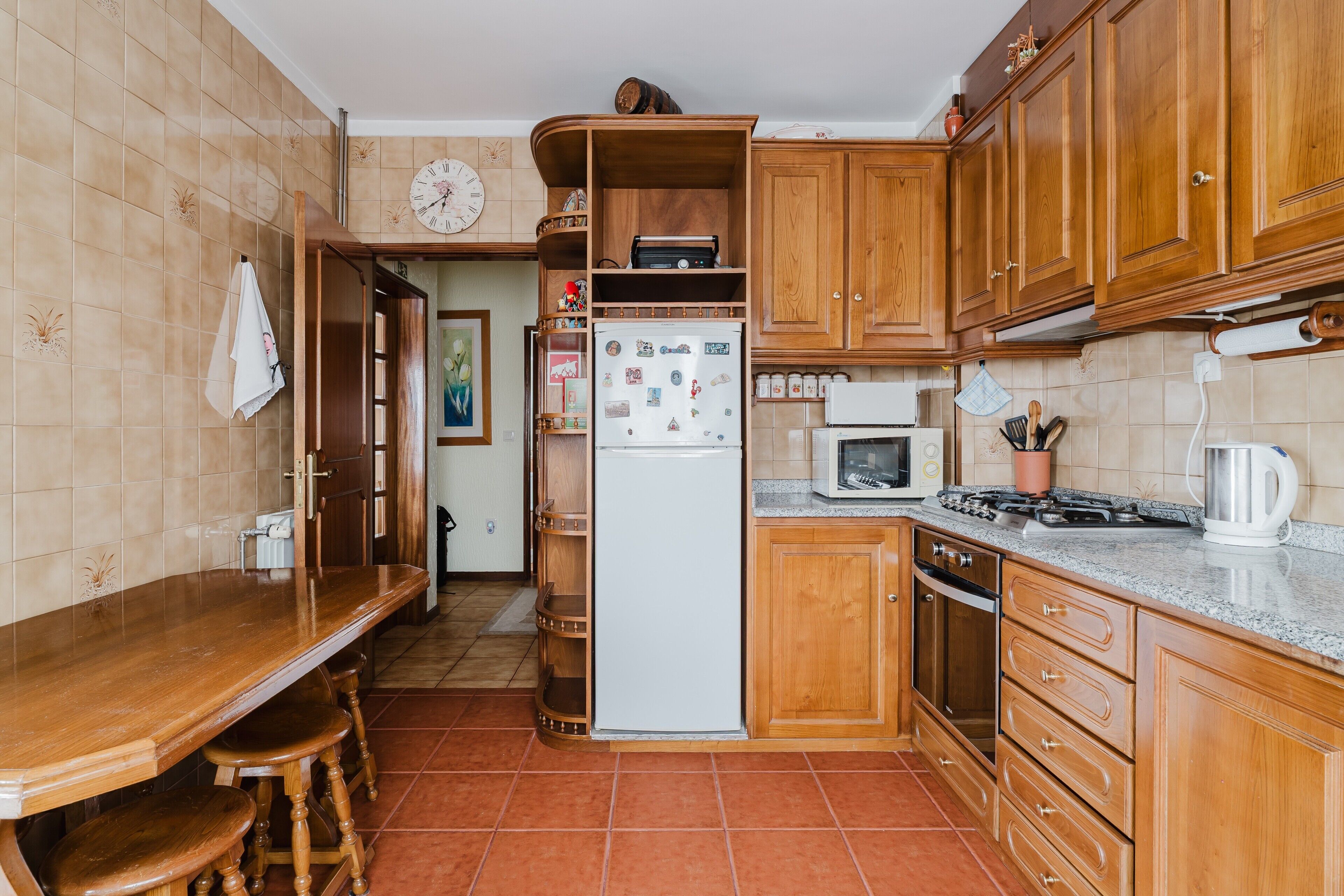 A kitchen with wooden cabinets, a refrigerator, a microwave, a stove, and a dining table with stools.