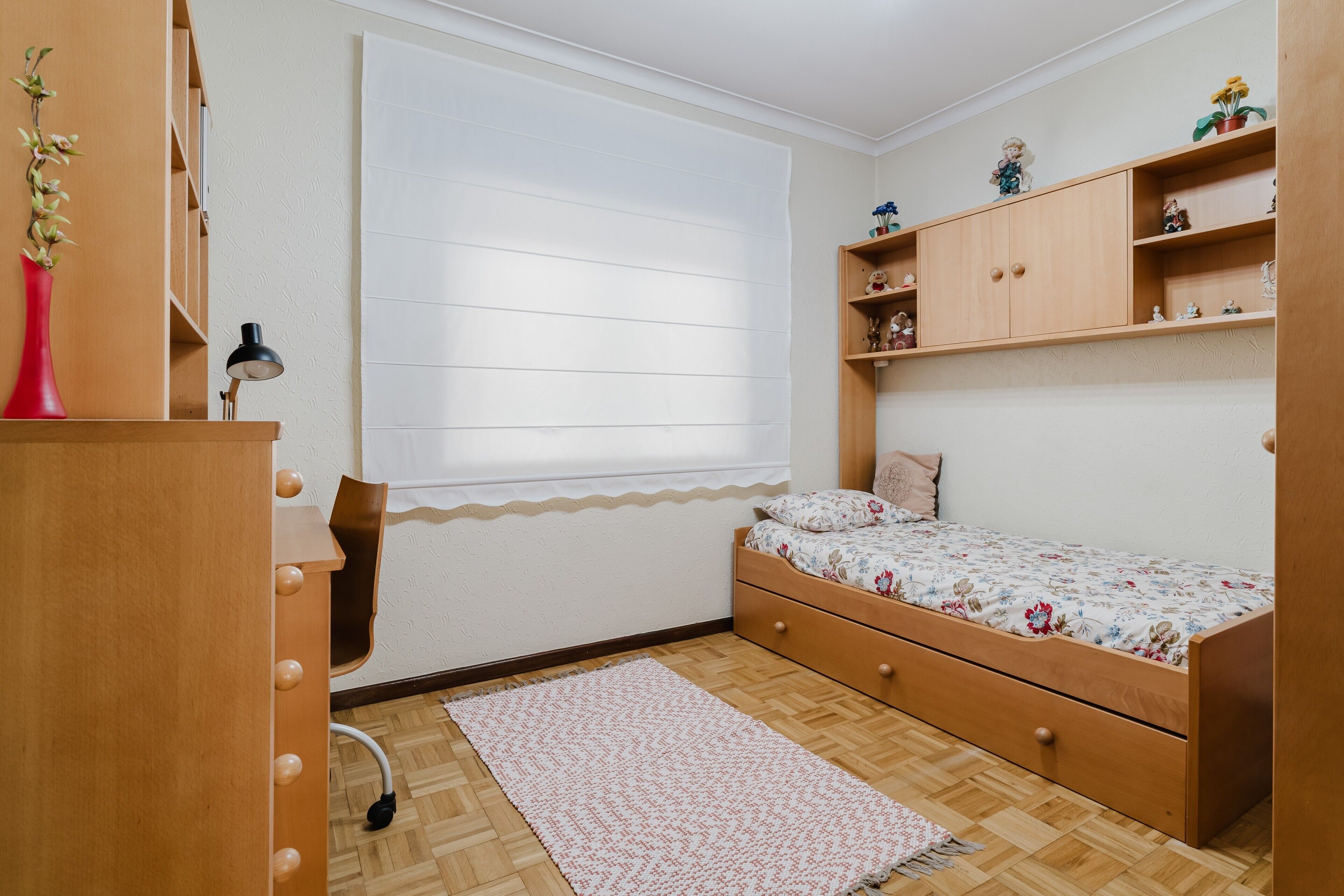 A bedroom with a bed, wooden dresser, shelves, and a window.