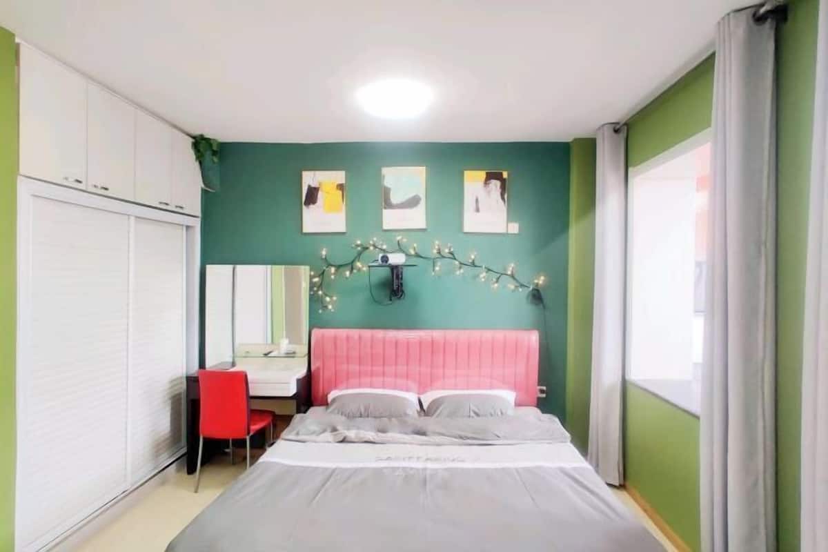 Une chambre à coucher avec un lit, un bureau, une chaise et une armoire. Il y a trois tableaux encadrés au mur et une guirlande lumineuse au-dessus du lit.