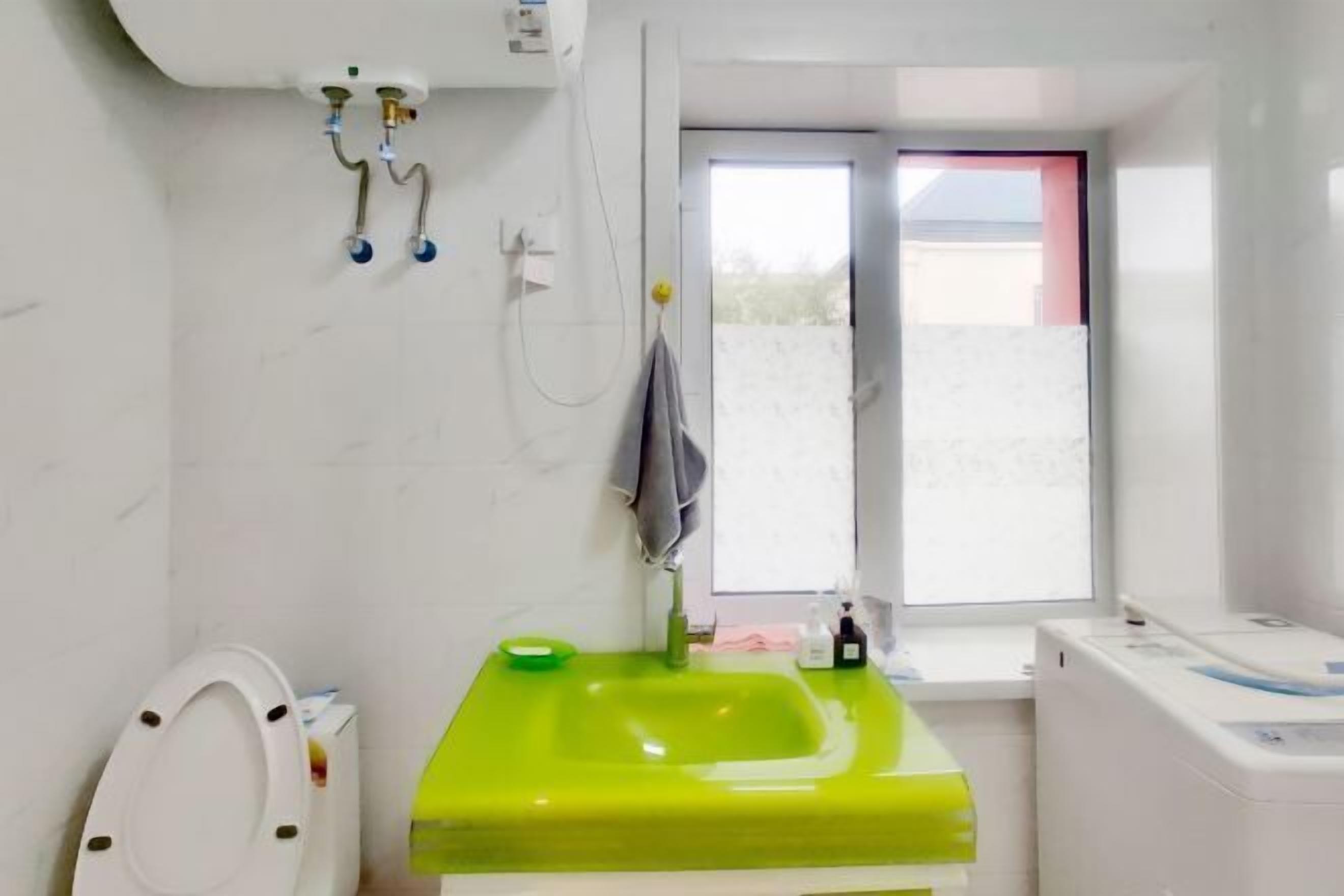 A bathroom with a green sink, a toilet, a window, and a washing machine.
