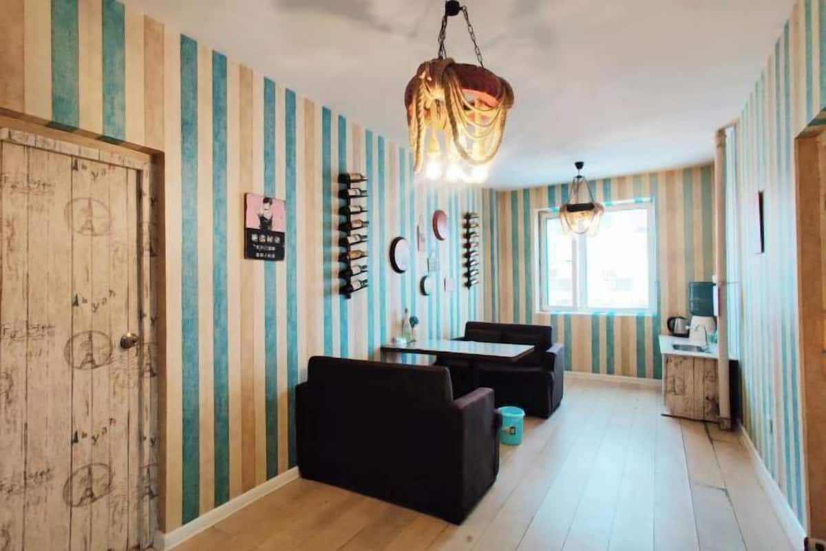 Une pièce avec un papier peint à rayures, une porte en bois, une table avec des chaises, un luminaire suspendu et une fenêtre.