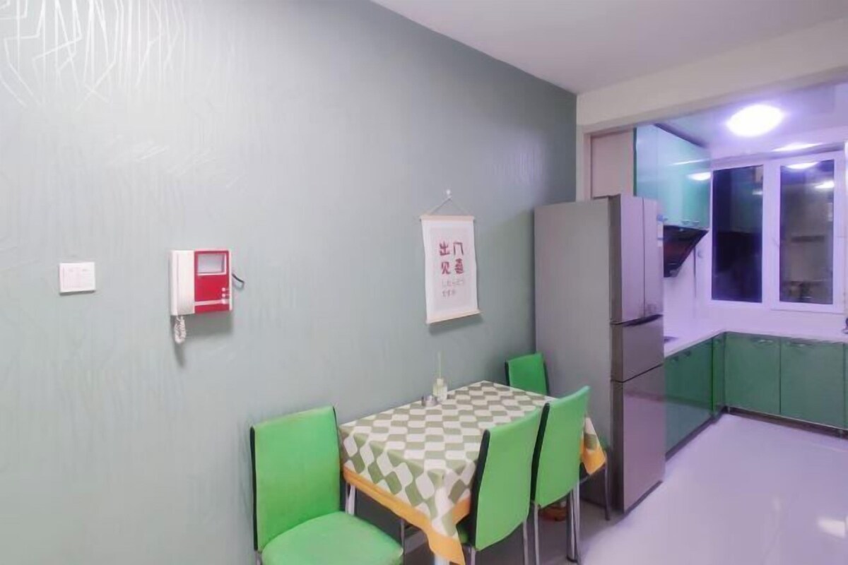 A dining area with a table and chairs, a refrigerator, and a kitchen visible through an open door.