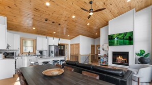 A spacious living area with a large wooden dining table, black leather sofa, and a fireplace. - Modern Mountain Lodge with a View (Fleetwood)