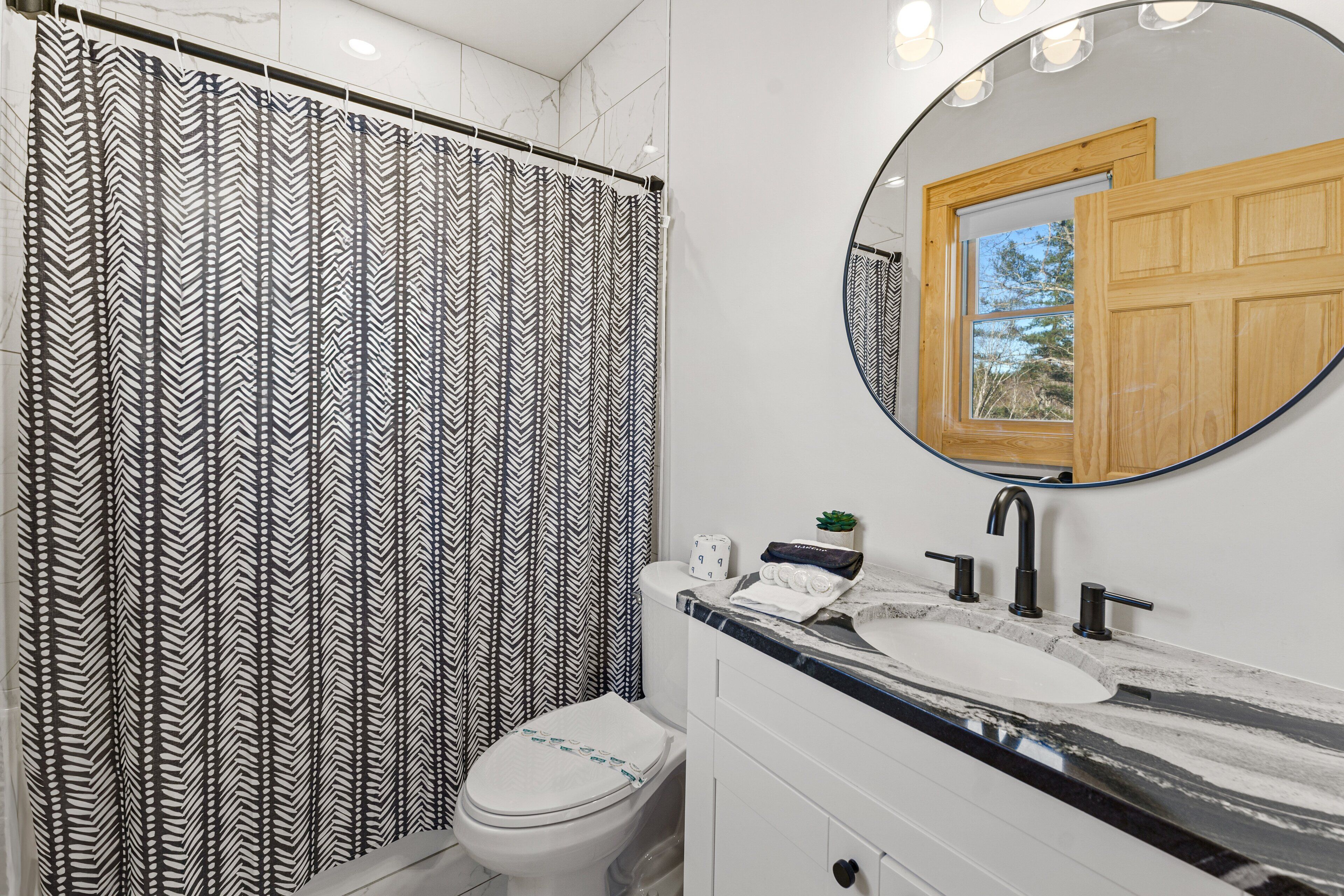 A bathroom with a black and white chevron shower curtain, a white toilet, a sink with a mirror above it, and a wooden door.